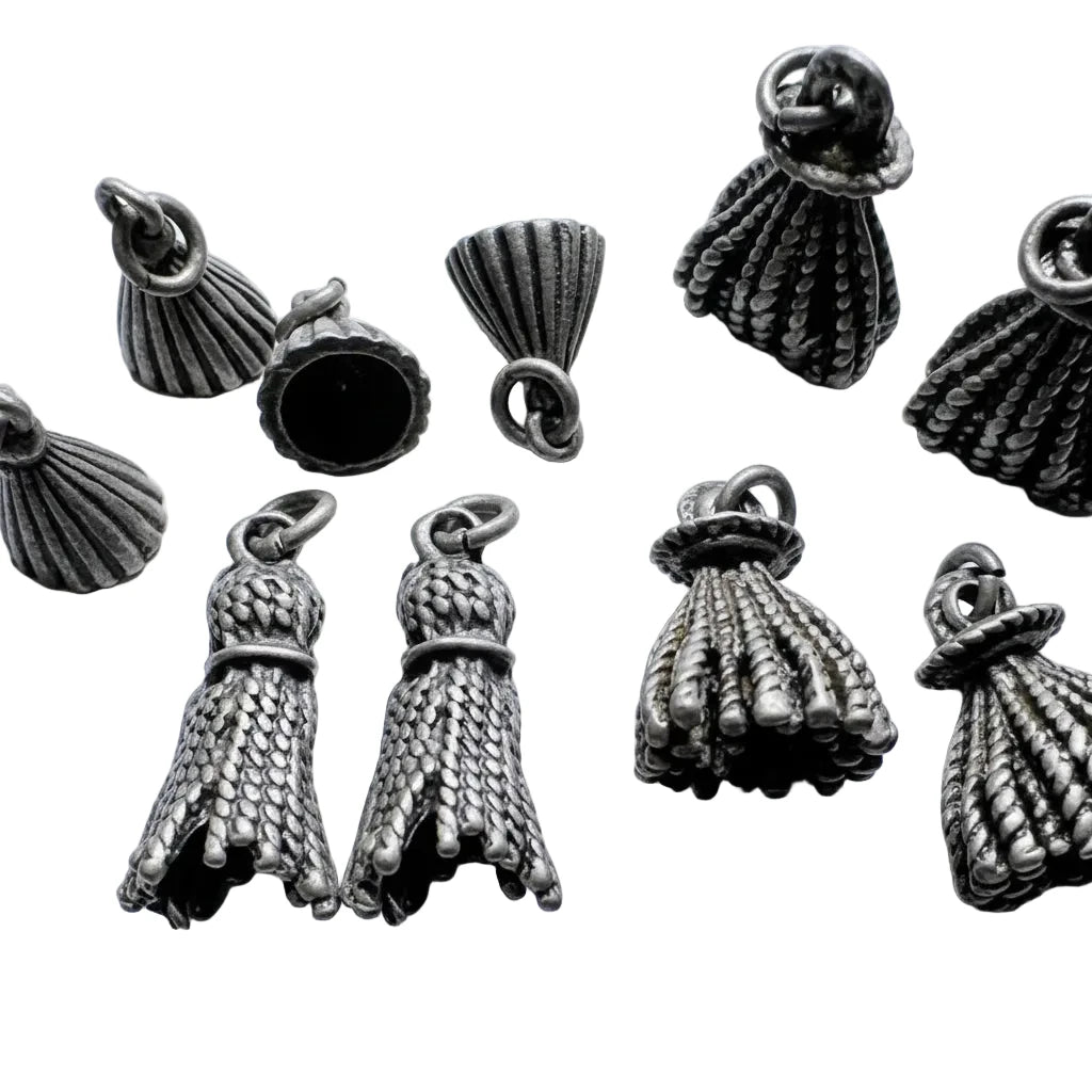 Several small metallic jewelry findings or charms with a textured, woven, or shell-like appearance are arranged on a light background. A coin is partially visible at the bottom right for scale.