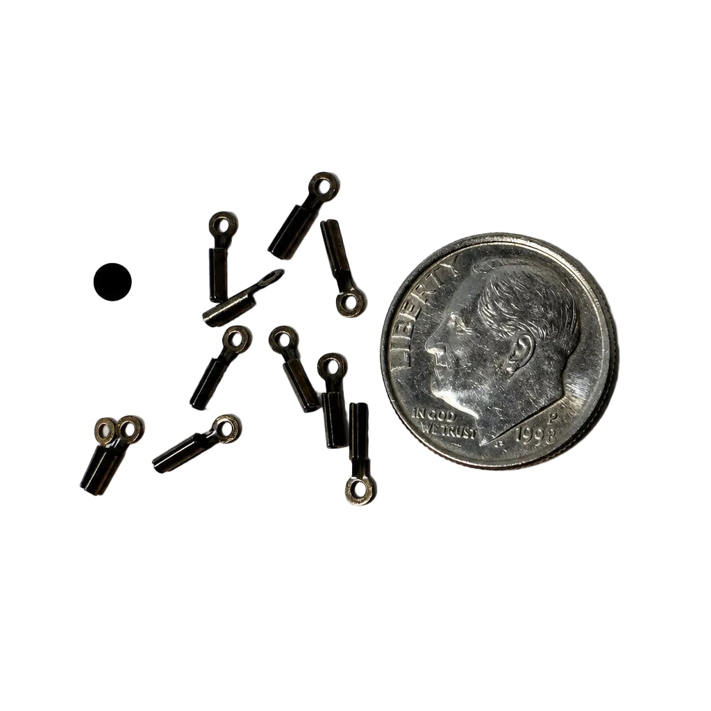 Several small black metal eyelet hardware pieces scattered on a white surface next to a U.S. dime for scale.