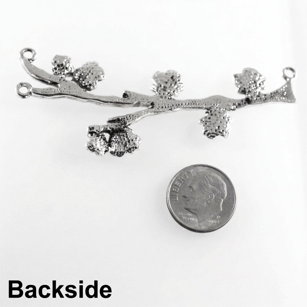 A silver-toned metal branch-shaped jewelry charm with textured leaf clusters and small hanging loops, shown on a white background next to a U.S.