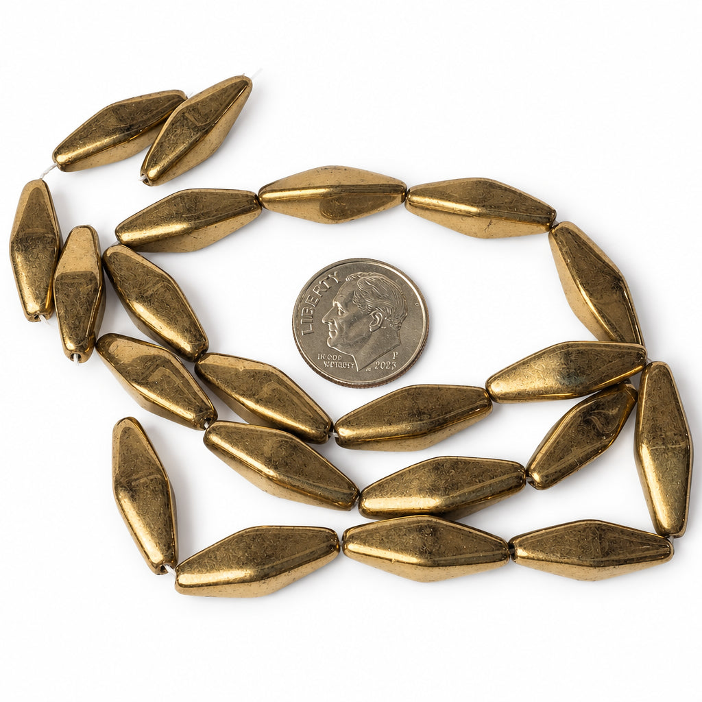 A strand of metallic gold-colored, elongated teardrop-shaped beads arranged in a loose circle around a US quarter coin for scale, on a plain white background.
