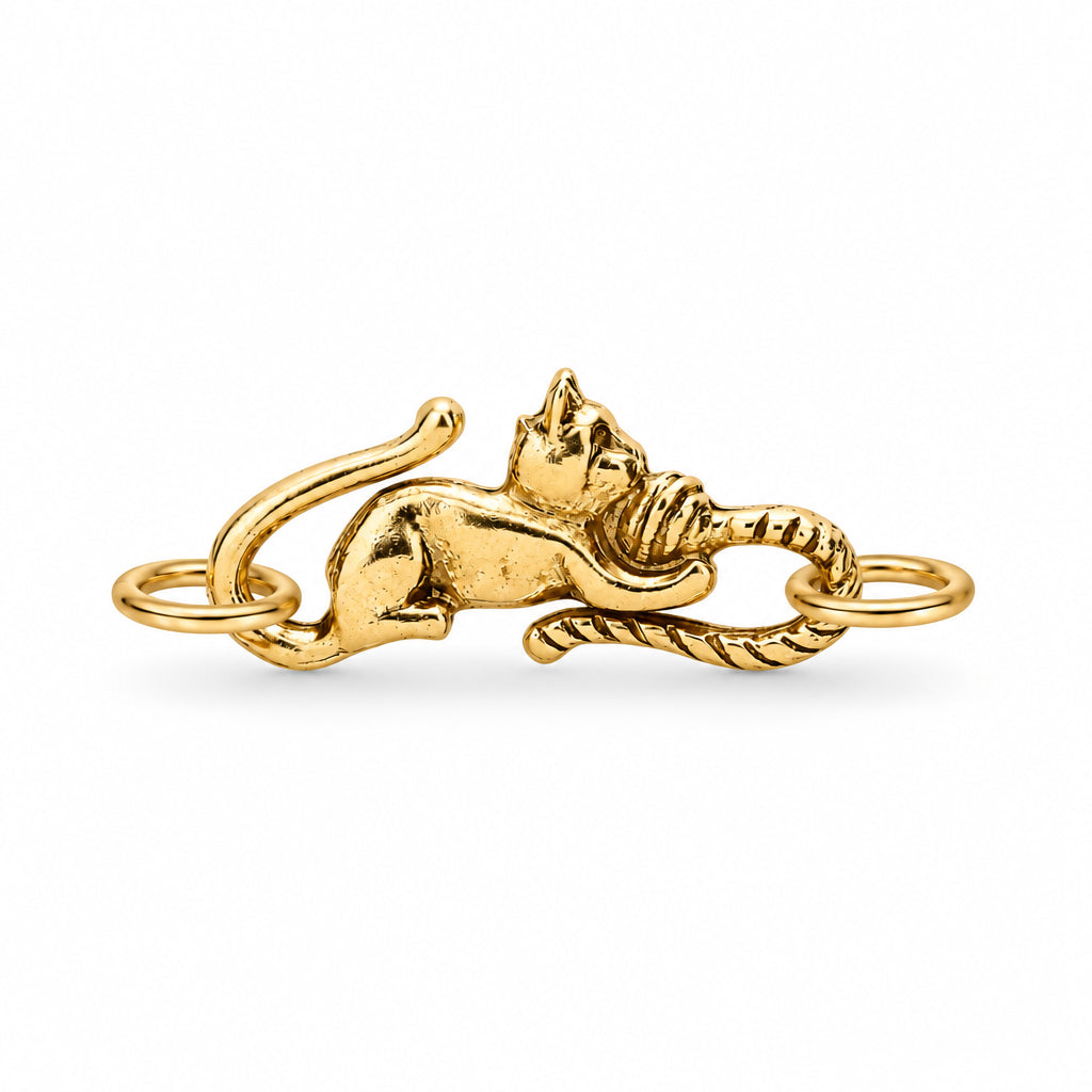 A gold-colored metal ring featuring a detailed sculpted cat lying down and biting a rope, set against a plain white background.