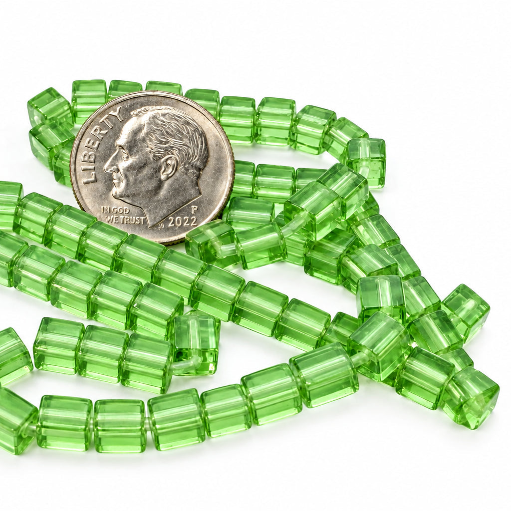 Green translucent rectangular beads scattered on a white surface, with a U.S. quarter coin placed on top for size reference.