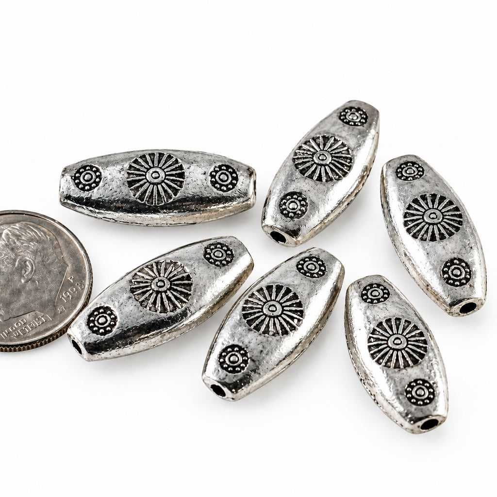 Five silver metallic oval beads with embossed sunburst and floral patterns, displayed on a white background next to a coin for scale.