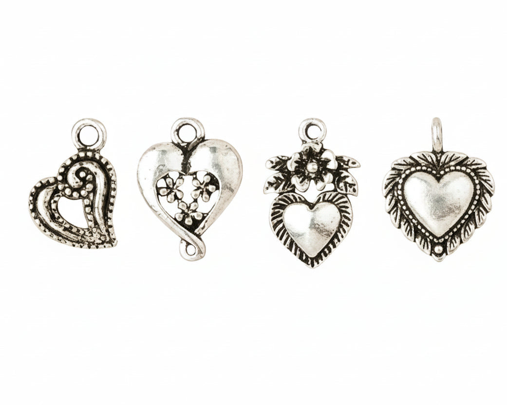 Four antique silver heart-shaped jewelry charms with intricate filigree and floral details, arranged horizontally on a plain white background.