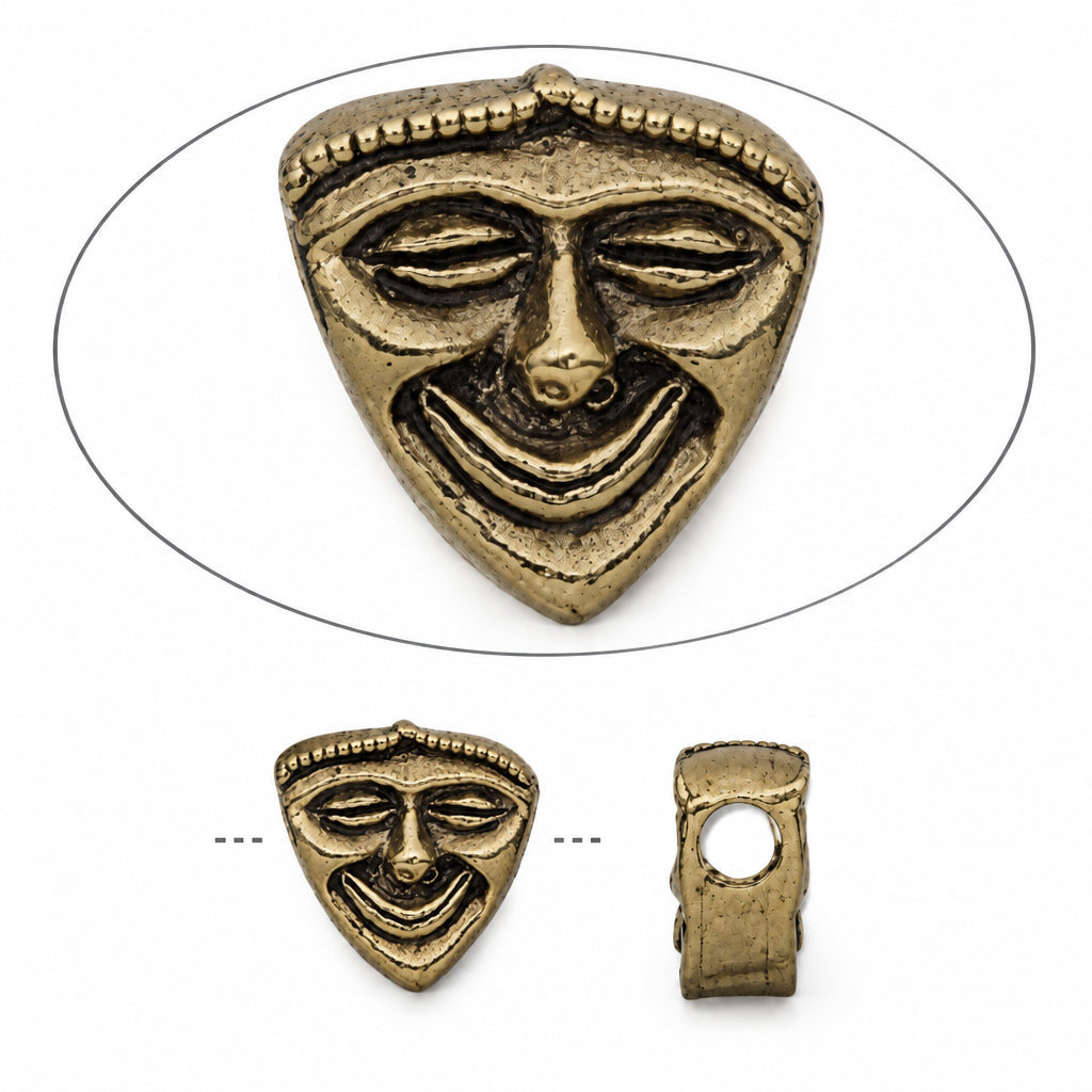 Gold-toned triangular bead with an engraved mask face design, shown from the front inside an oval outline, plus two smaller views below showing the back and side profile on a white background.