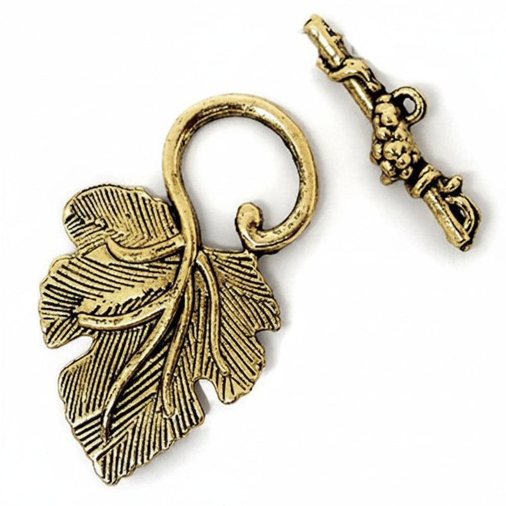 An antique gold leaf-shaped pendant charm with a loop, shown next to its matching key-shaped clasp on a plain white background.