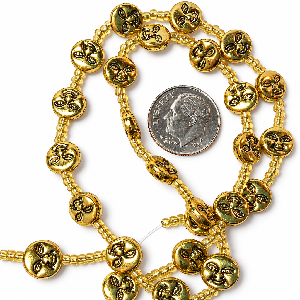 Gold-colored beaded necklace featuring round beads with a fleur-de-lis pattern, shown next to a US dime for scale on a white background.