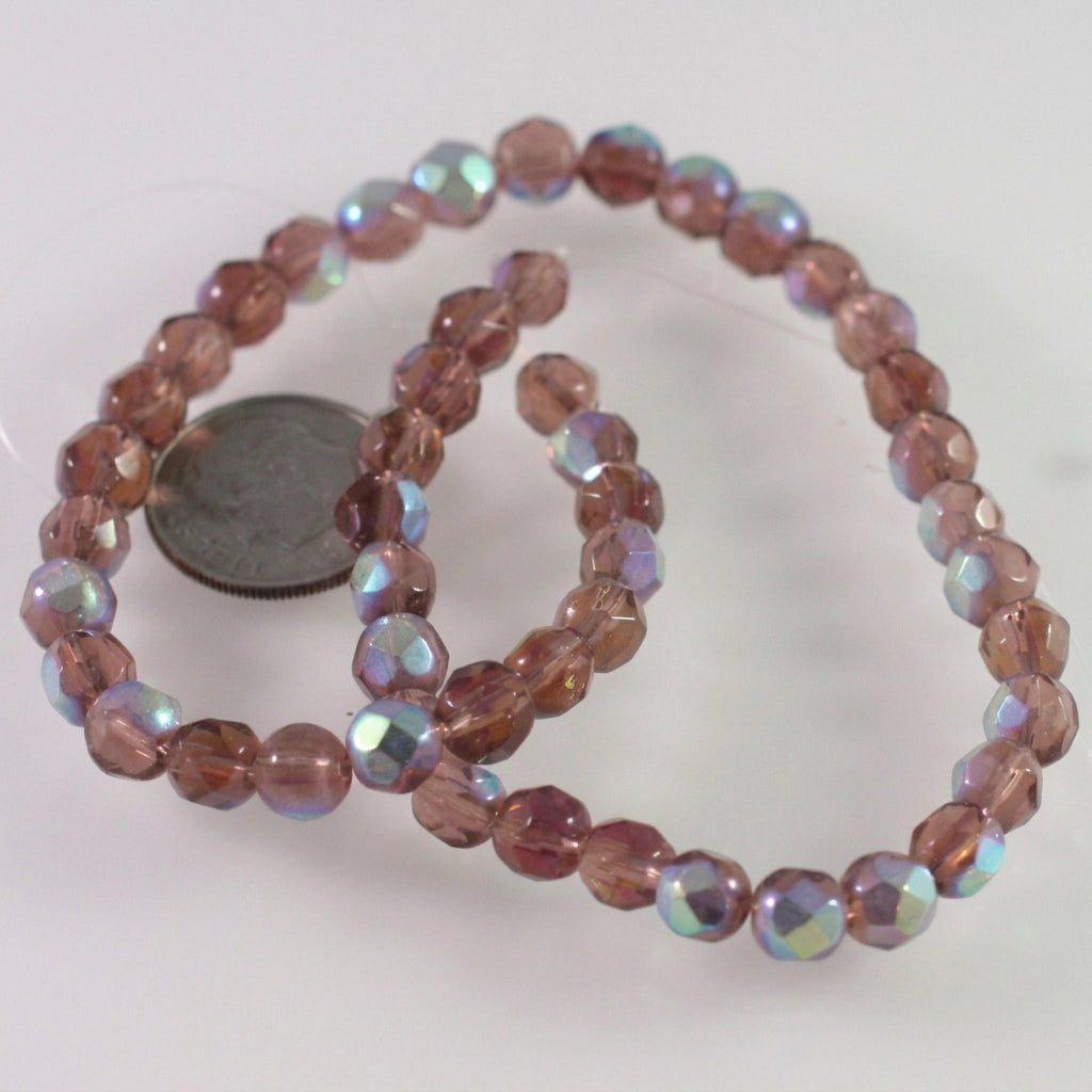 A strand of faceted round beads in a dusty rose pink color with an iridescent AB finish, shown next to a US quarter for scale on a white background.