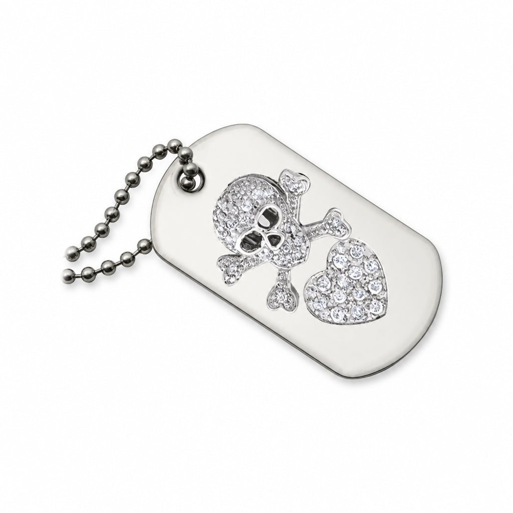 A silver-toned dog tag necklace featuring a skull and crossbones design embellished with clear rhinestones, alongside a heart-shaped crystal cluster, on a white background.