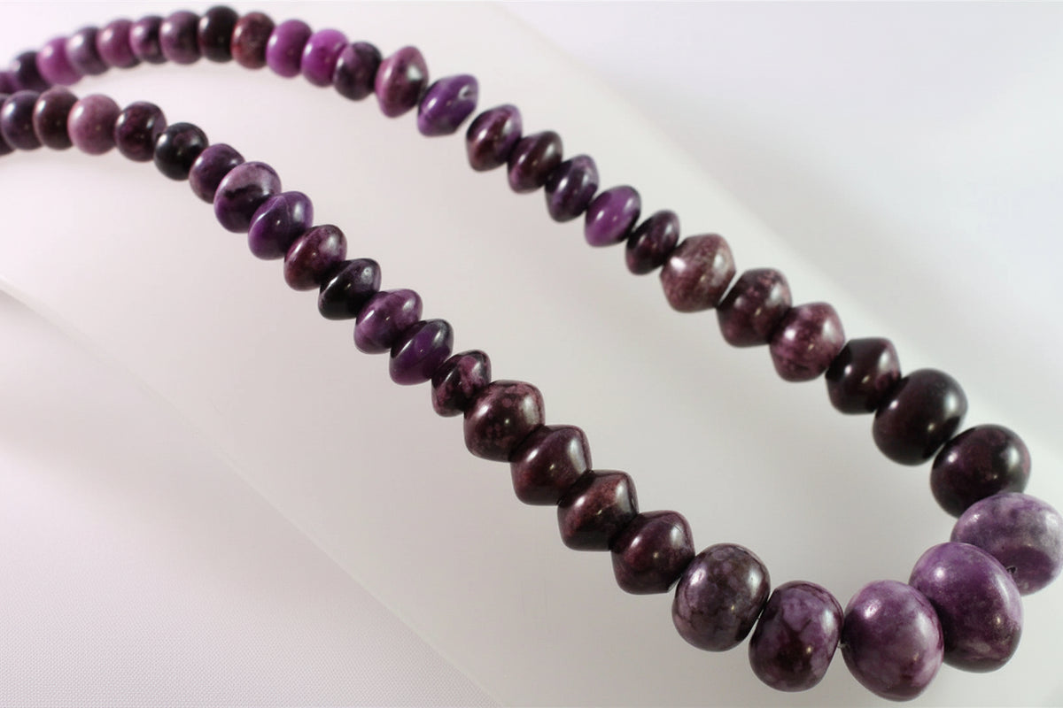A strand of polished purple and dark maroon beads, likely hematite or a similar stone, arranged in two loops on a white background.