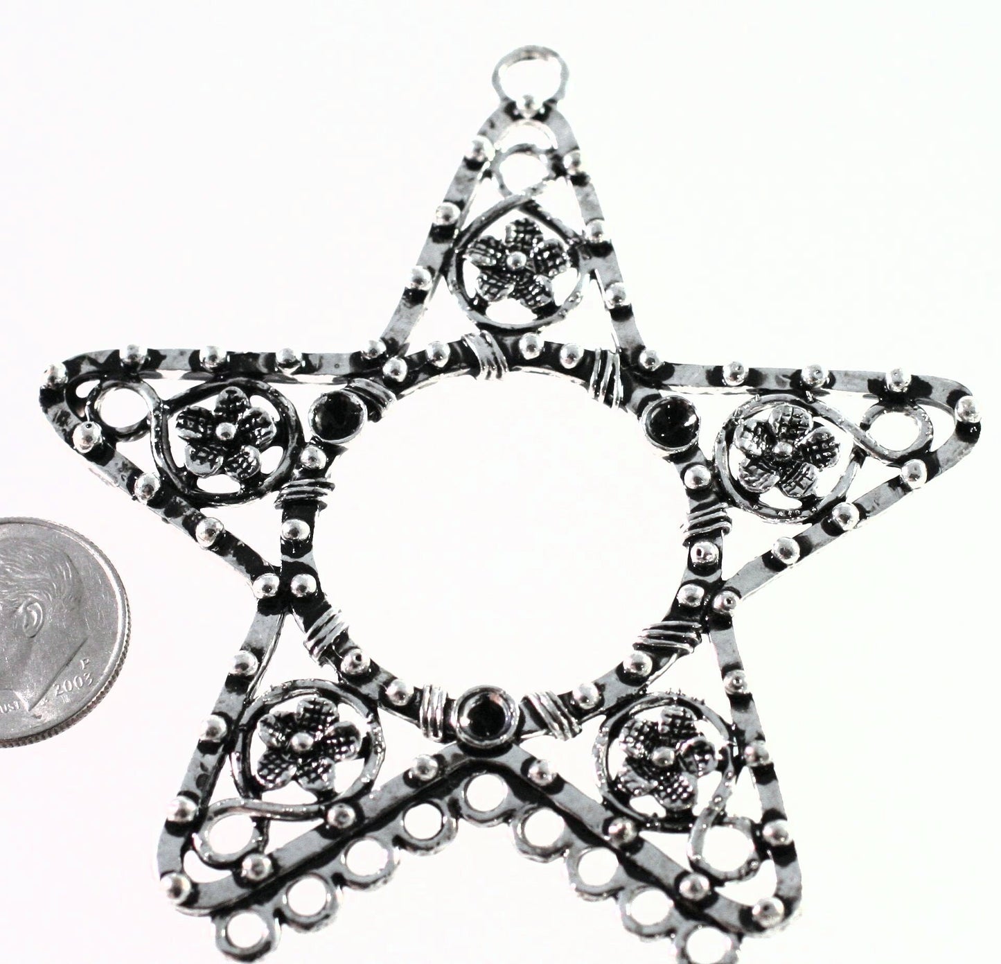 Star-shaped silver pendant with intricate designs on a white background, next to a coin for scale.
