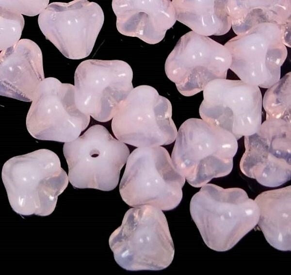 A pile of small translucent pale pink beads with a floral or clover-like shape, shown on a black background.