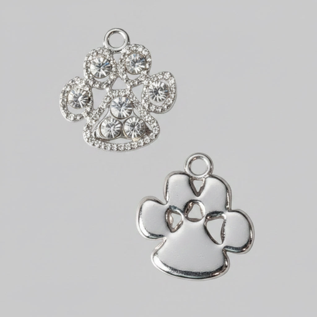 Two silver paw print charms on a light gray background, one embellished with clear rhinestones and the other with a textured metallic finish.