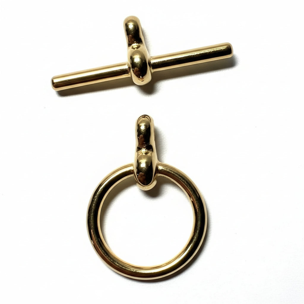 Two small gold-tone jewelry findings on a white surface: a toggle clasp at the top and a ring pull at the bottom, with a U.S.
