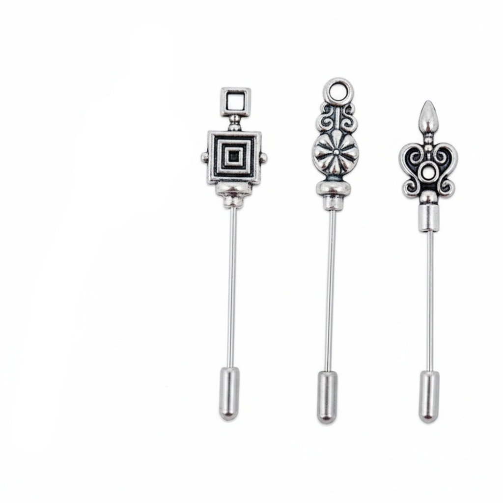 Four silver-toned metal pinback brooches with decorative tops, including a fleur-de-lis, a square medallion, an ornate floral motif, and a scrollwork design, shown on a plain white background.
