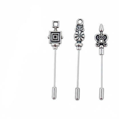 Four silver-toned metal pinback brooches with decorative tops, including a fleur-de-lis, a square medallion, an ornate floral motif, and a scrollwork design, shown on a plain white background.