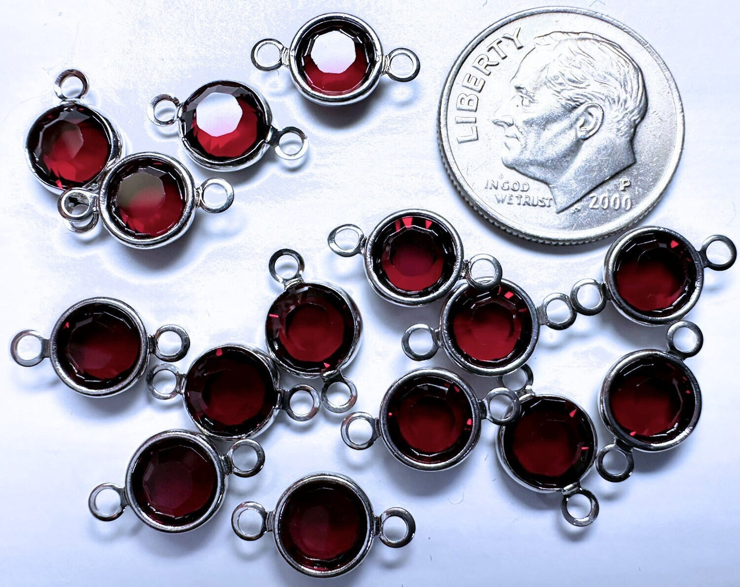 Silver pendants with red stones next to a dime for size comparison on a white background