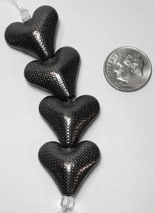 Stack of black heart-shaped objects with a quarter for scale on a white background