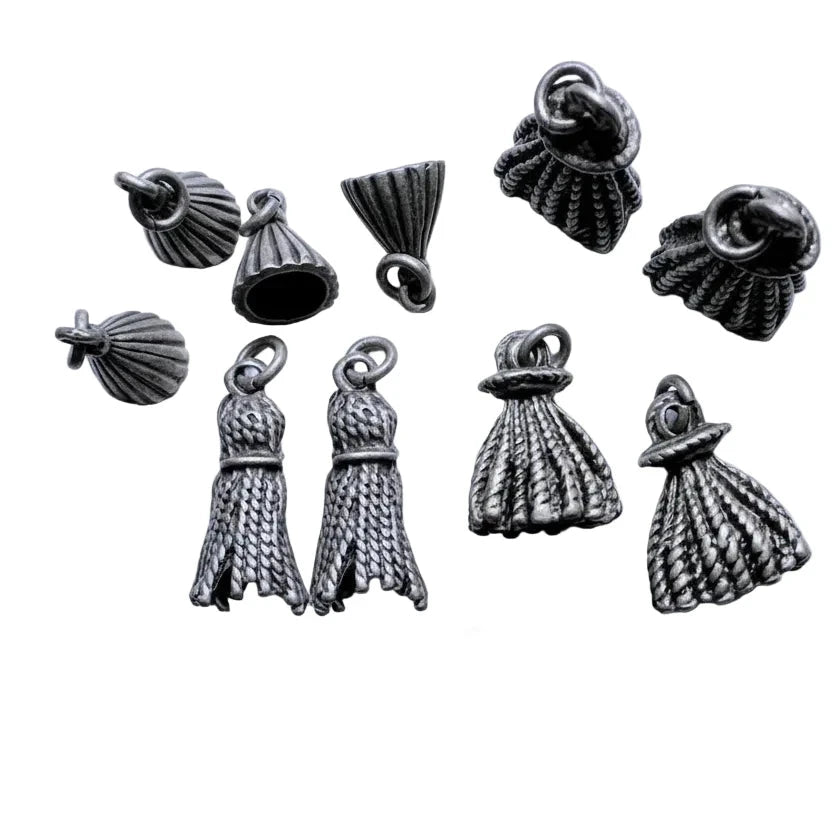 A set of nine silver-toned metallic dress-shaped charms with textured rope-like detailing and loop tops, arranged on a light background with a coin for scale.