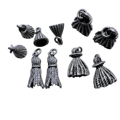 A set of nine silver-toned metallic dress-shaped charms with textured rope-like detailing and loop tops, arranged on a light background with a coin for scale.