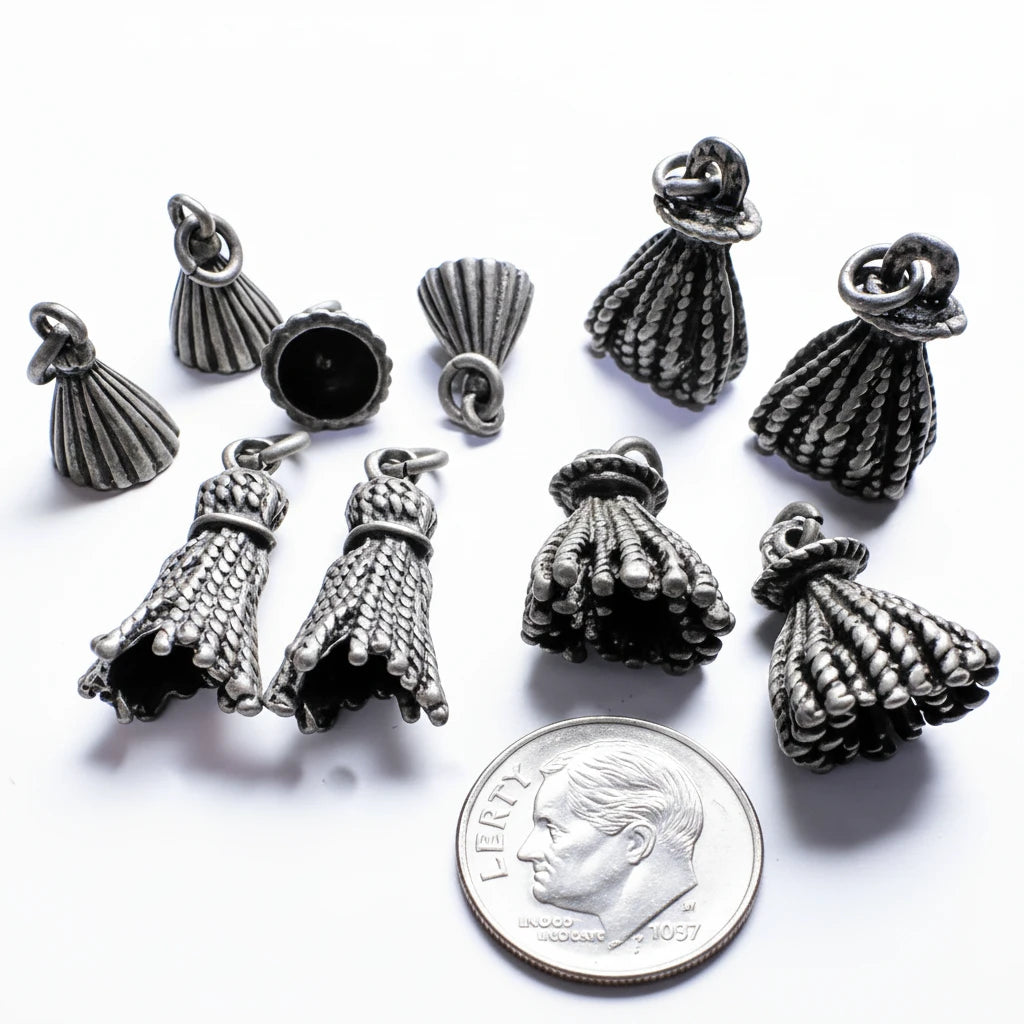 Several small metallic jewelry charms shaped like textured tassel or bell-like drops are arranged on a plain white background, with a coin at the bottom for scale.