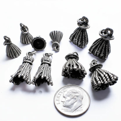 Several small metallic jewelry charms shaped like textured tassel or bell-like drops are arranged on a plain white background, with a coin at the bottom for scale.
