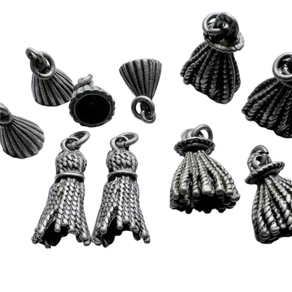 Several small metallic jewelry findings or charms with a textured, woven, or shell-like appearance are arranged on a light background. A coin is partially visible at the bottom right for scale.