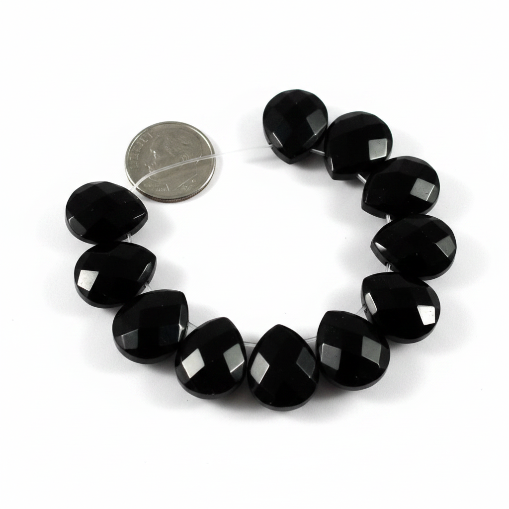 A strand of faceted black teardrop beads on a clear thread, shown next to a silver coin for scale on a white background.