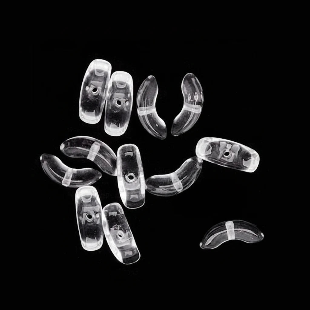 A set of clear, transparent curved plastic beads or spacer pieces scattered on a solid black background, with one piece shown separately in the upper left with a dashed guide line.
