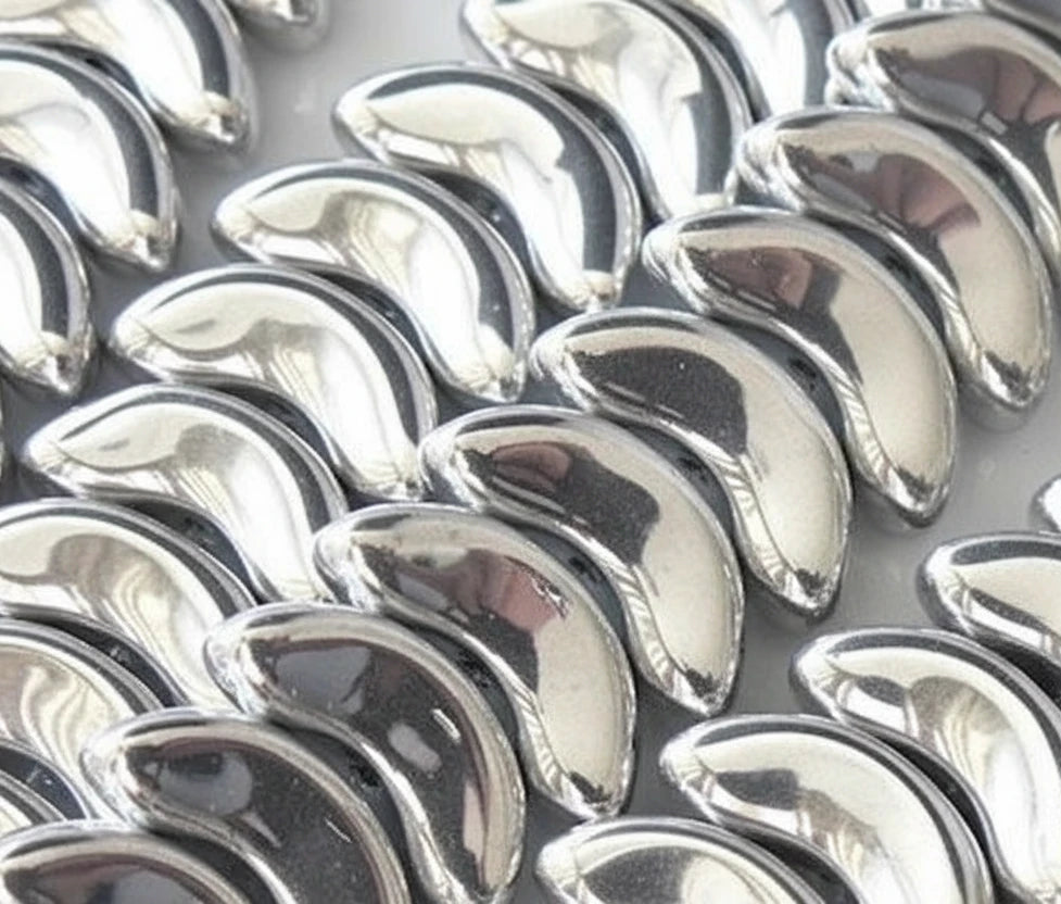 A close-up of multiple shiny metallic silver crescent-shaped pieces arranged in rows on a light background.