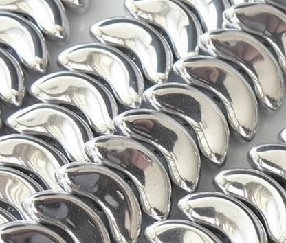 A close-up of multiple shiny metallic silver crescent-shaped pieces arranged in rows on a light background.