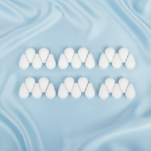 Sixteen white silicone droplet-style hair extension tips arranged in two rows of eight on a light blue satin fabric background.