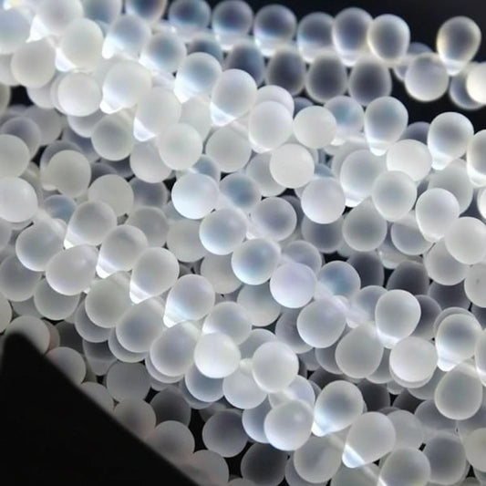 A close-up pile of small, translucent white plastic pellets or beads with a frosted, milky appearance.