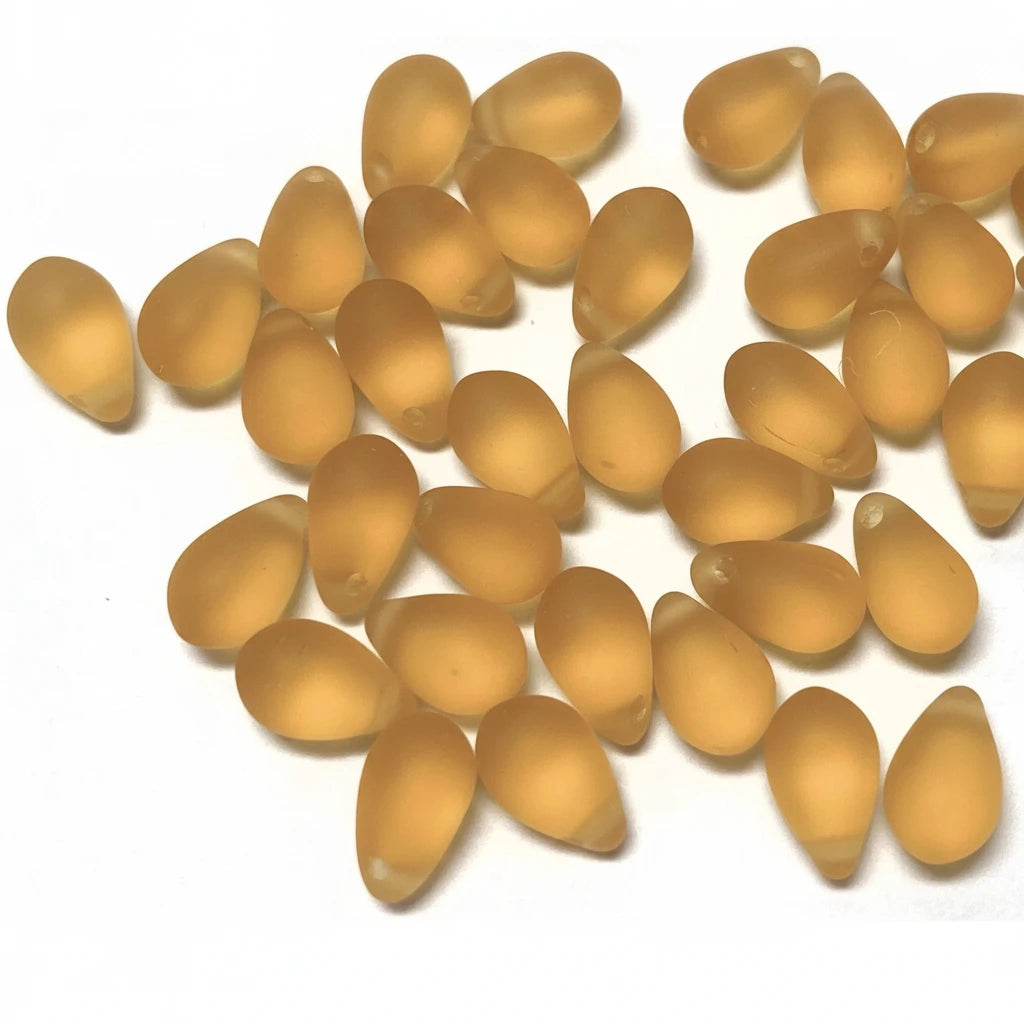 A pile of small, teardrop-shaped translucent amber or honey-colored beads scattered on a plain white background.