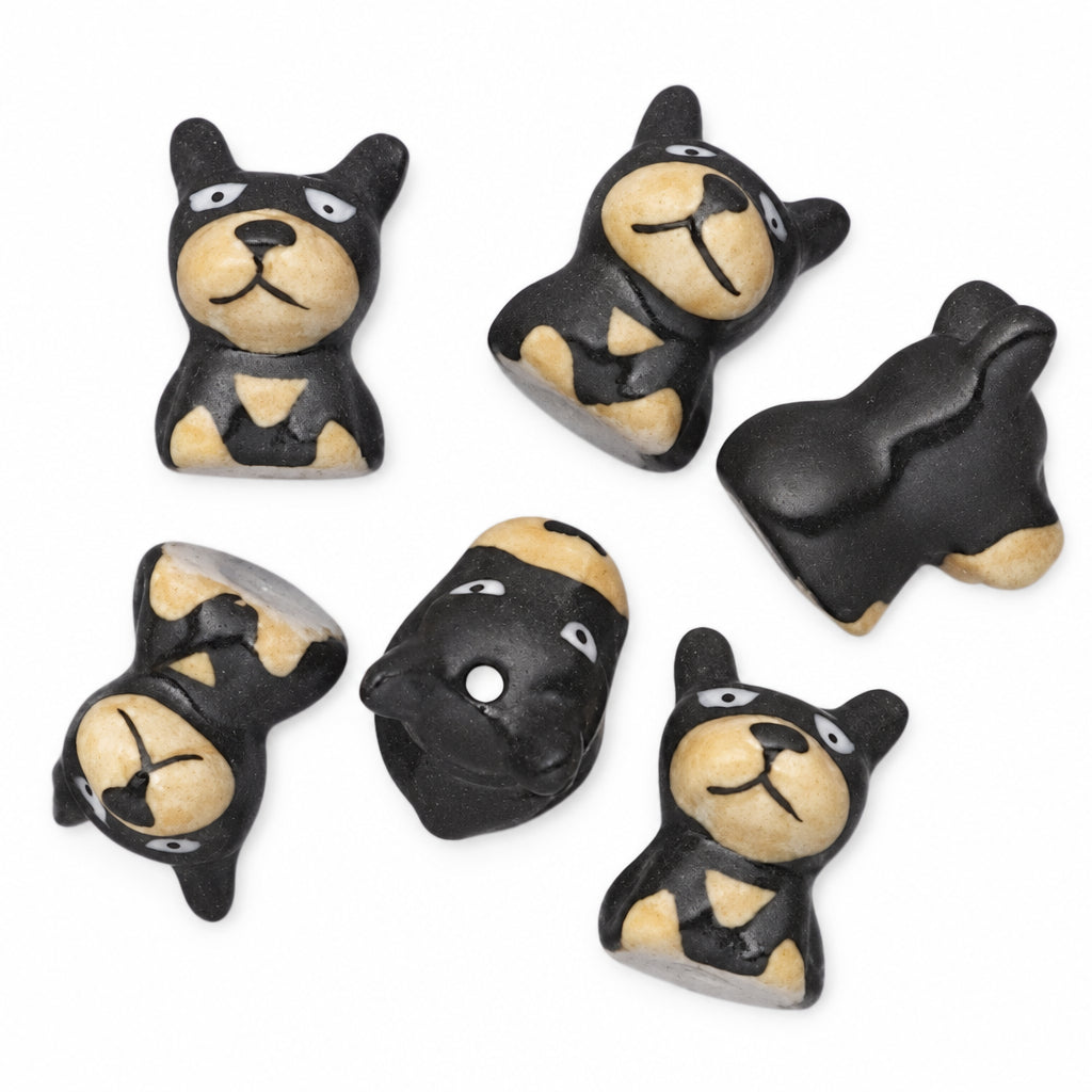 Six small black and tan dog-shaped beads or charms arranged on a plain white background.