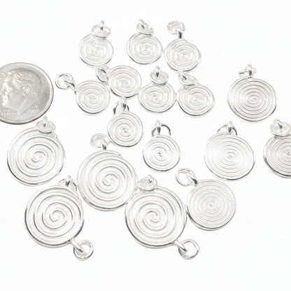 Multiple silver spiral pendant charms arranged on a white background, with a U.S. DIME coin included for size reference.