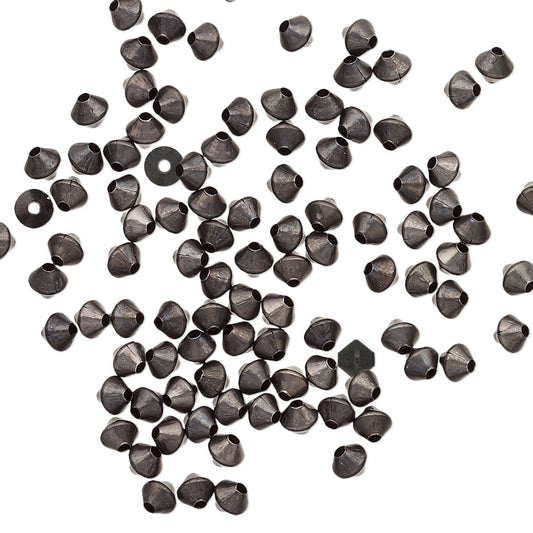 A scattered pile of small metallic dark gunmetal gray beads with a hexagonal shape and a central hole, arranged on a plain white background.