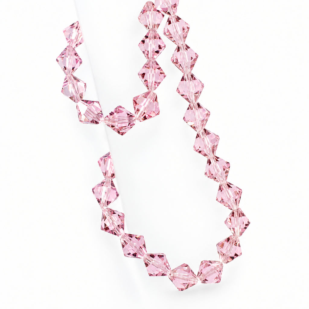 A strand of faceted light pink crystal beads draped over a translucent display stand against a pale background.