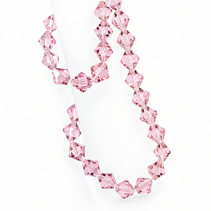 A strand of faceted light pink crystal beads draped over a translucent display stand against a pale background.