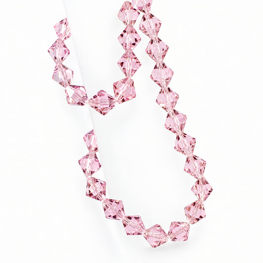 A strand of faceted light pink crystal beads draped over a translucent display stand against a pale background.
