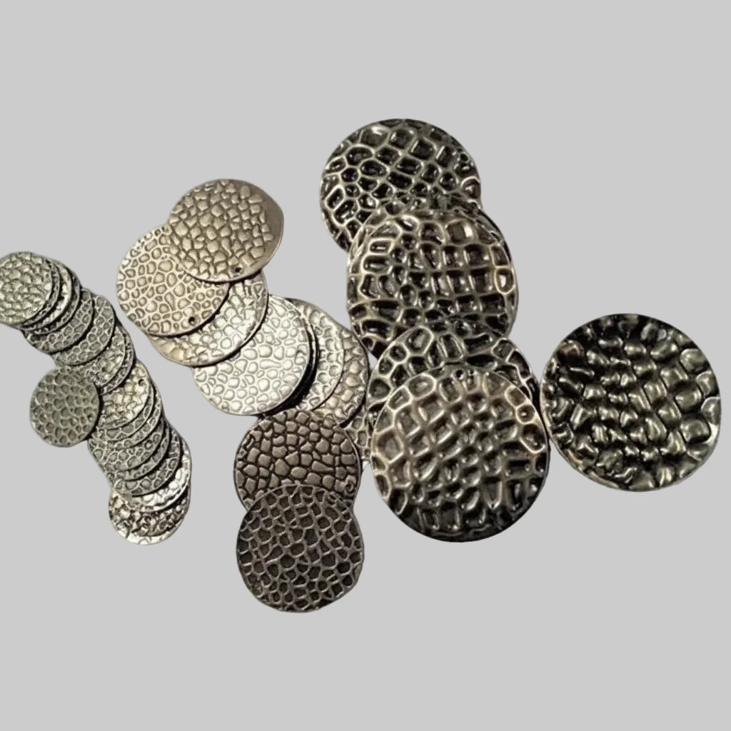 A group of round metal buttons with textured finishes, including hammered, dimpled, and wavy patterns, displayed on a light gray textured background.