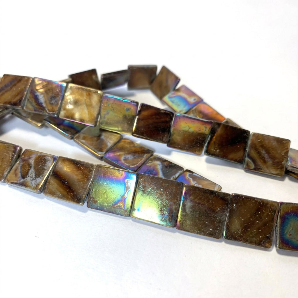 Square glass beads with a dark brown base and an iridescent, rainbow-like sheen of blue, green, and gold, arranged on a white background.