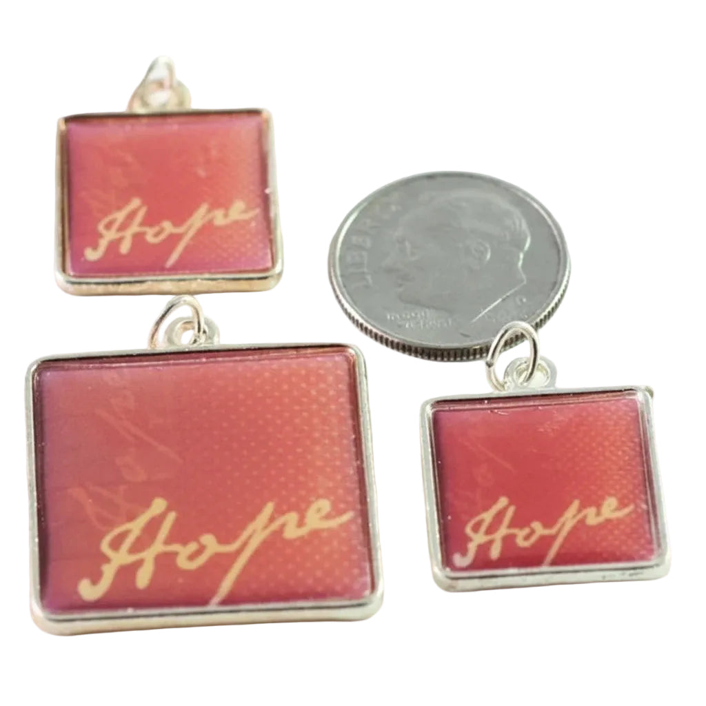 Three square red and pink jewelry charms with the word 'Hope' in gold script, shown alongside a silver coin for scale on a white background.
