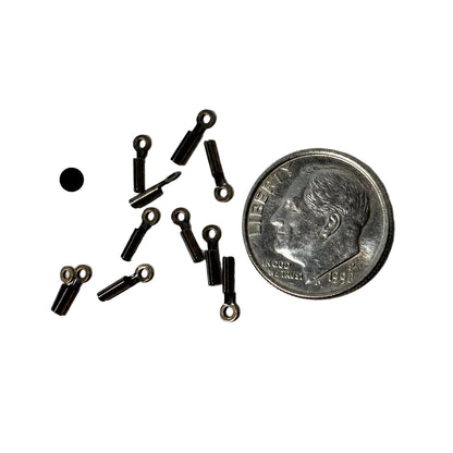 Several small black metal eyelet hardware pieces scattered on a white surface next to a U.S. dime for scale.