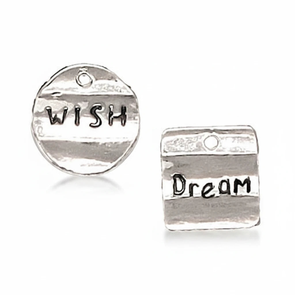 Two silver-toned metal charms on a light gray background. One round charm is stamped with the word 'WISH' and one rectangular charm is stamped with 'Dream'.