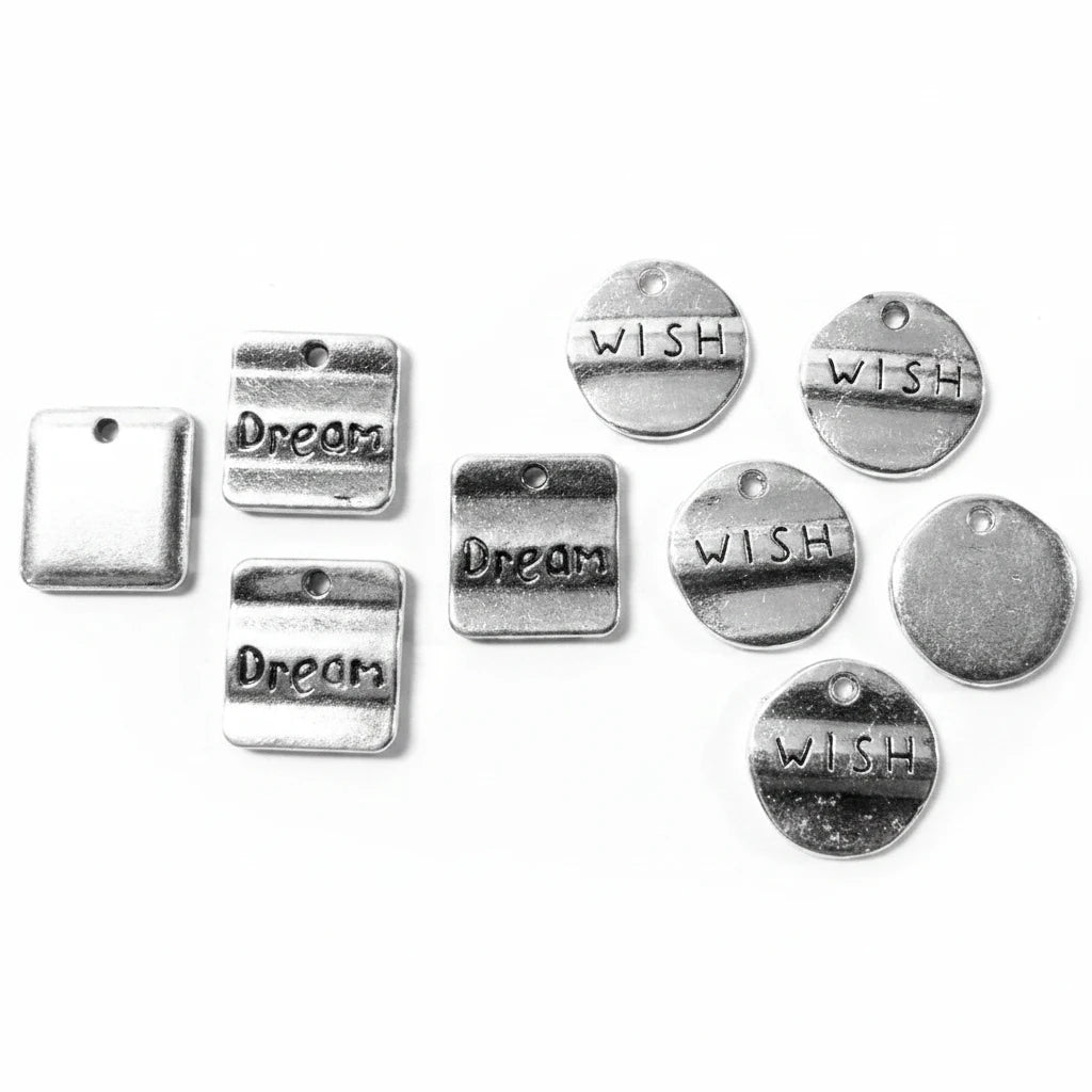 A set of silver-toned metal charms on a light gray background, including rectangular tags with the words 'Dream' and round discs with the word 'WISH'.