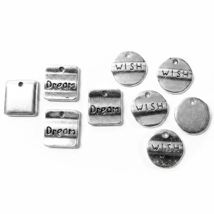 A set of silver-toned metal charms on a light gray background, including rectangular tags with the words 'Dream' and round discs with the word 'WISH'.