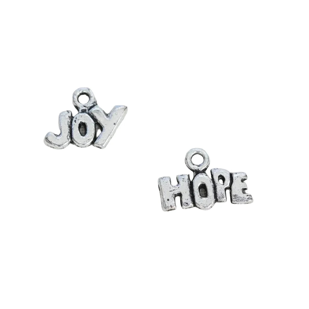 Two small silver-toned metal charms spelling 'JOY' and 'HOPE' on a brown textured fabric background, with the text 'The Mystical Garden Path' printed below.