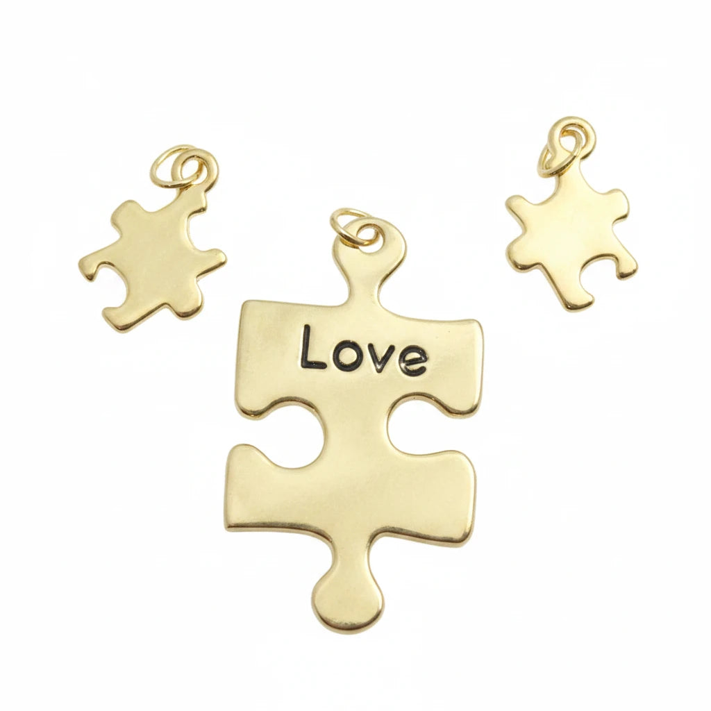 Three gold-toned puzzle piece charms on a light blue textured background, with the center charm engraved with the word 'Love' and a watermark reading 'TheMysticalGardenPath' across the bottom.