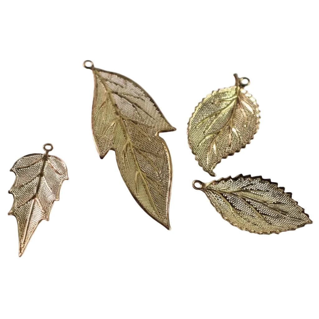 Four gold-toned metal leaf-shaped charms with textured mesh details and small hanging loops, arranged on a plain white background.